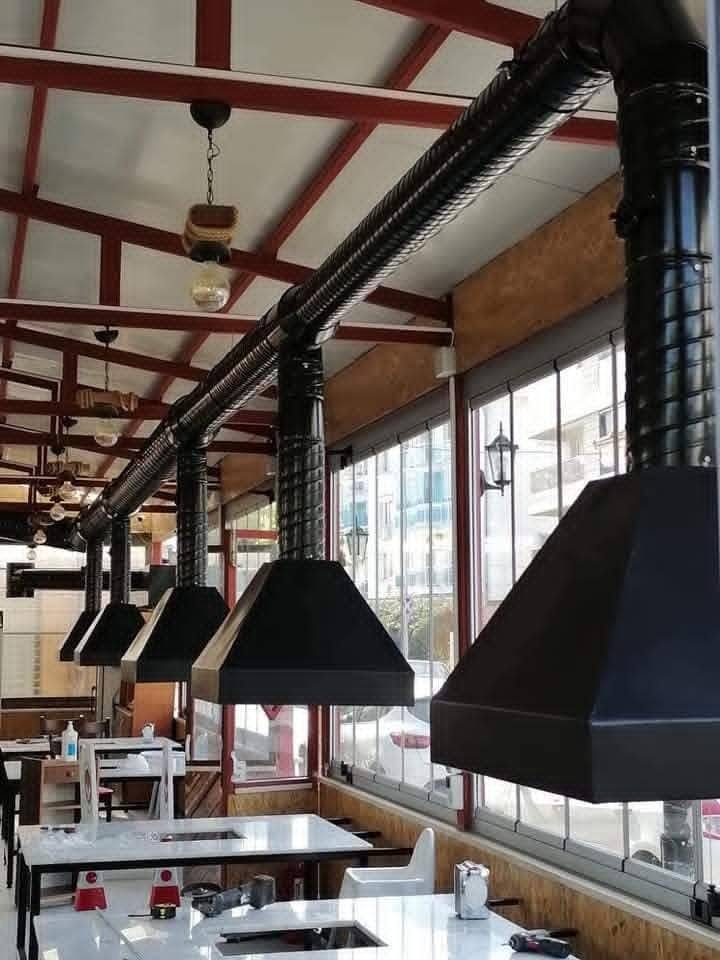 Restoranda her masanın üzerinde siyah boyalı davlumbaz ve tavan egzoz kanalı